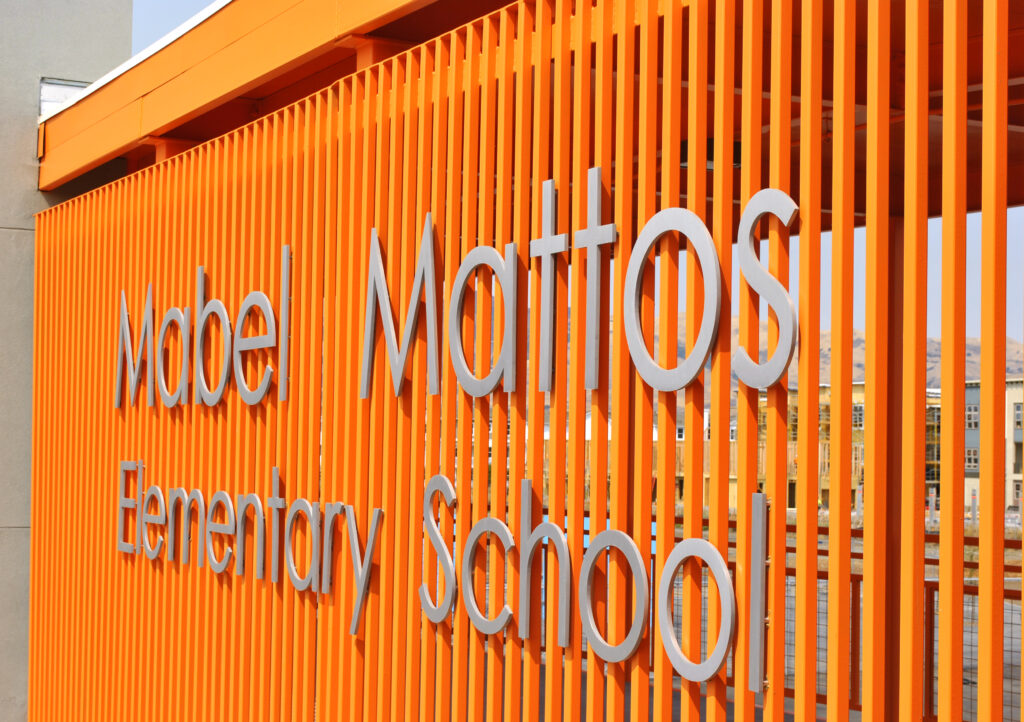 Close-up of the Mabel Mattos Elementary School sign with bold orange design on the exterior of the building.