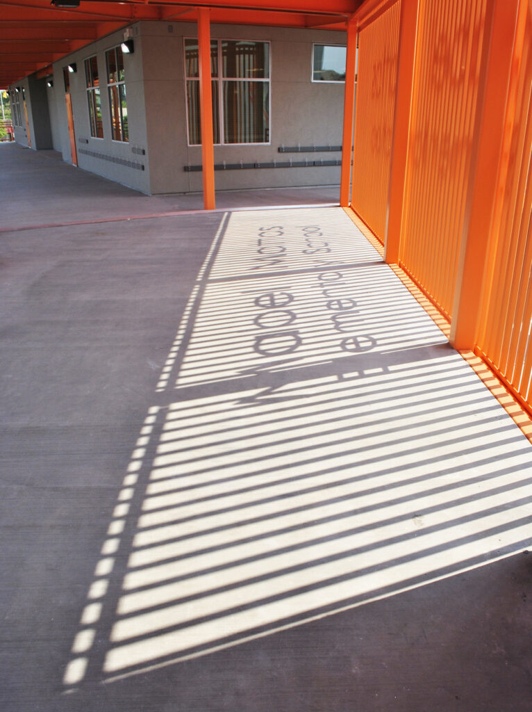 Unique shadow cast by the Mabel Mattos Elementary School sign onto the pavement, highlighting the modern orange design.