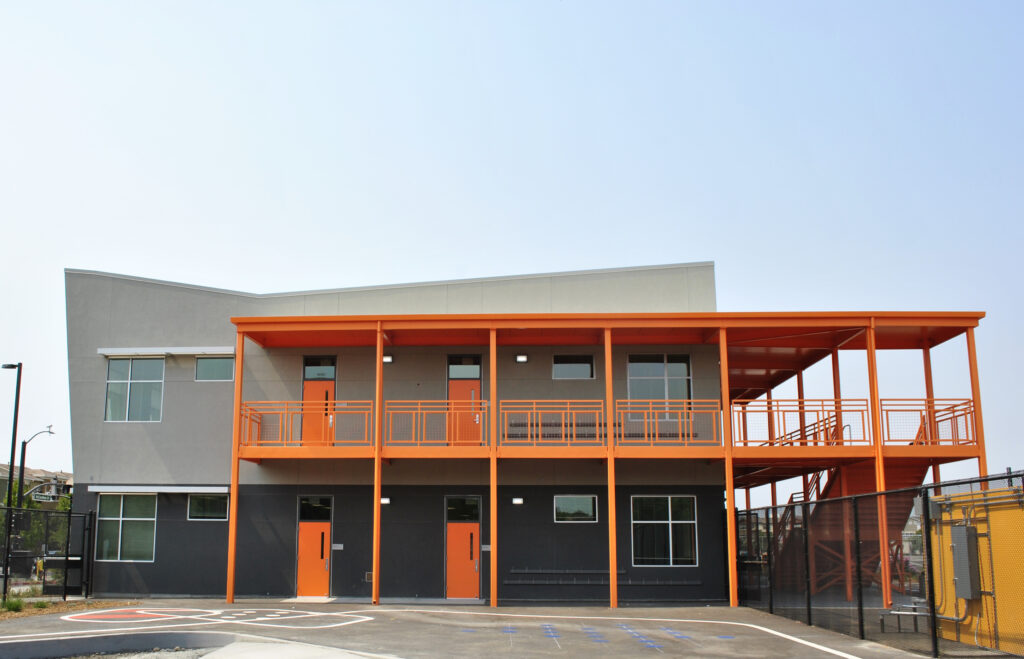 Rear view of the two-story classroom building at Mabel Mattos Elementary School with bright orange exterior elements.