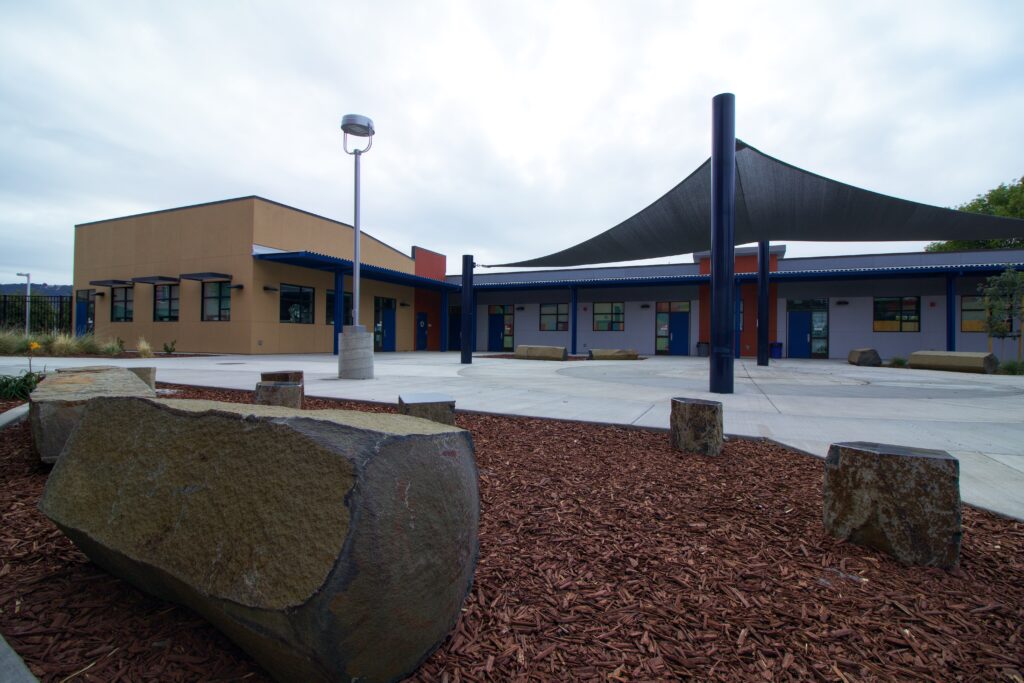 Exterior of the Hart Middle School science building, with outdoor courtyard seating and shade structures for students.